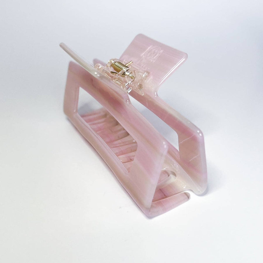 
A translucent, pale pink hair claw clip with a visible metal spring is angled on a white background.