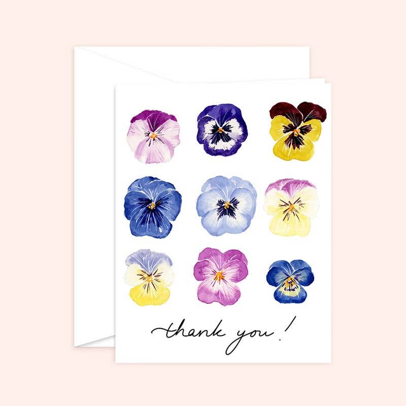 Watercolor greeting card and white envelope featuring a grid of nine vibrant pansies in shades of purple, blue, and yellow with the handwritten text "thank you!"