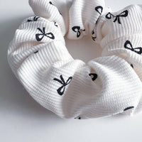 Thumbnail for Close up of a white scrunchie with a ribbed texture, patterned with small black bow-tie shapes.