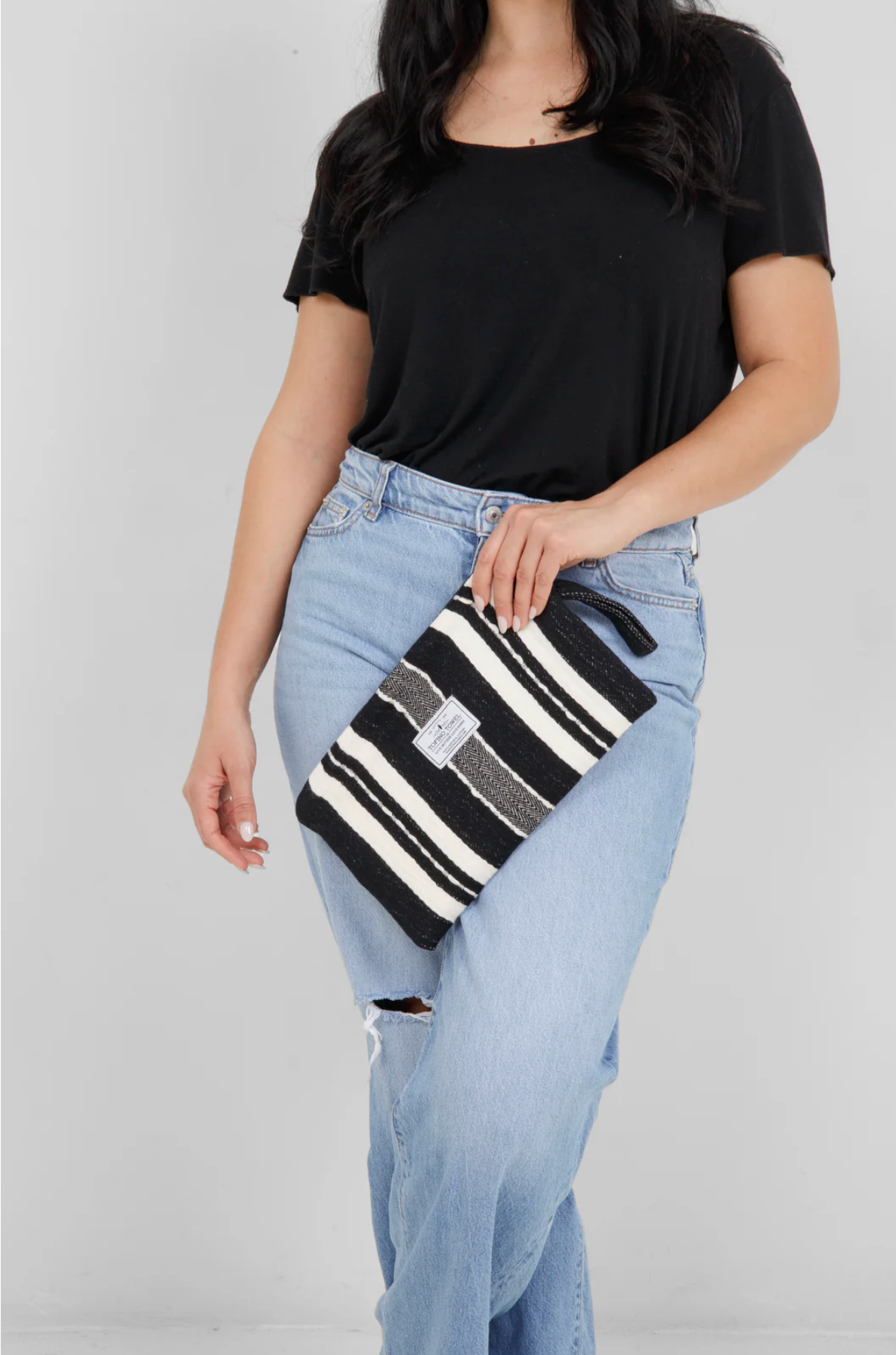 A person holding the small Black/Ecru striped Mercer bag at their side, showing the wrist strap and the bag's size relative to the body.