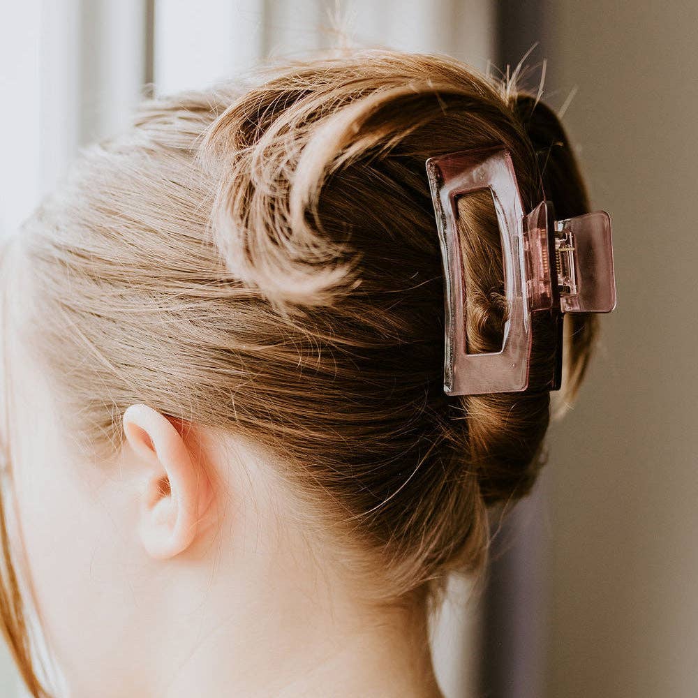 A person with light brown hair has a section of their hair held back with a small, square, translucent pink claw clip.