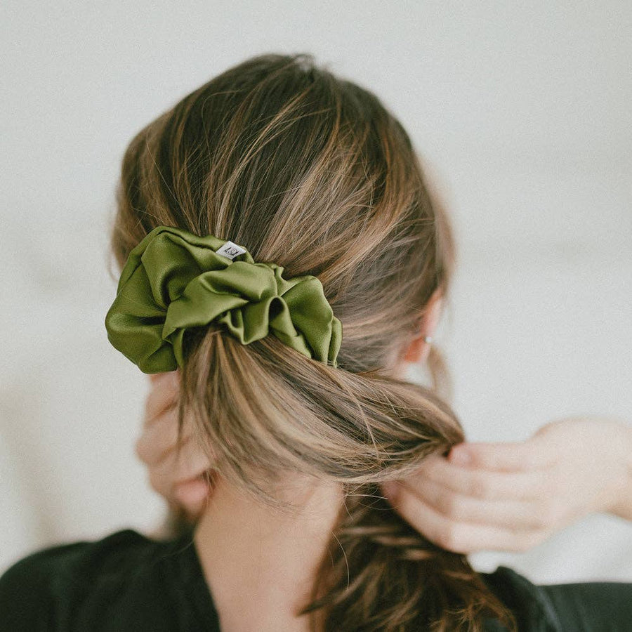 A olive/khaki coloured silk scrunchie in a ponytail of a person with long light brown hair. 