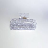 Thumbnail for 
A translucent, marbled grey and white hair claw clip is resting on a white surface, viewed from the front.