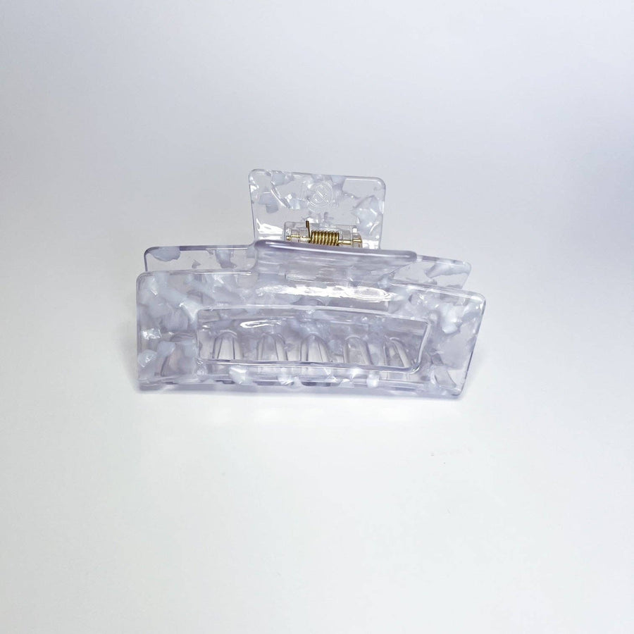 
A translucent, marbled grey and white hair claw clip is resting on a white surface, viewed from the front.