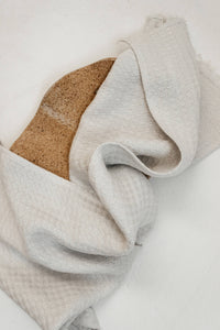 Thumbnail for Folded light gray towel on a white surface folded over a wooden plate.