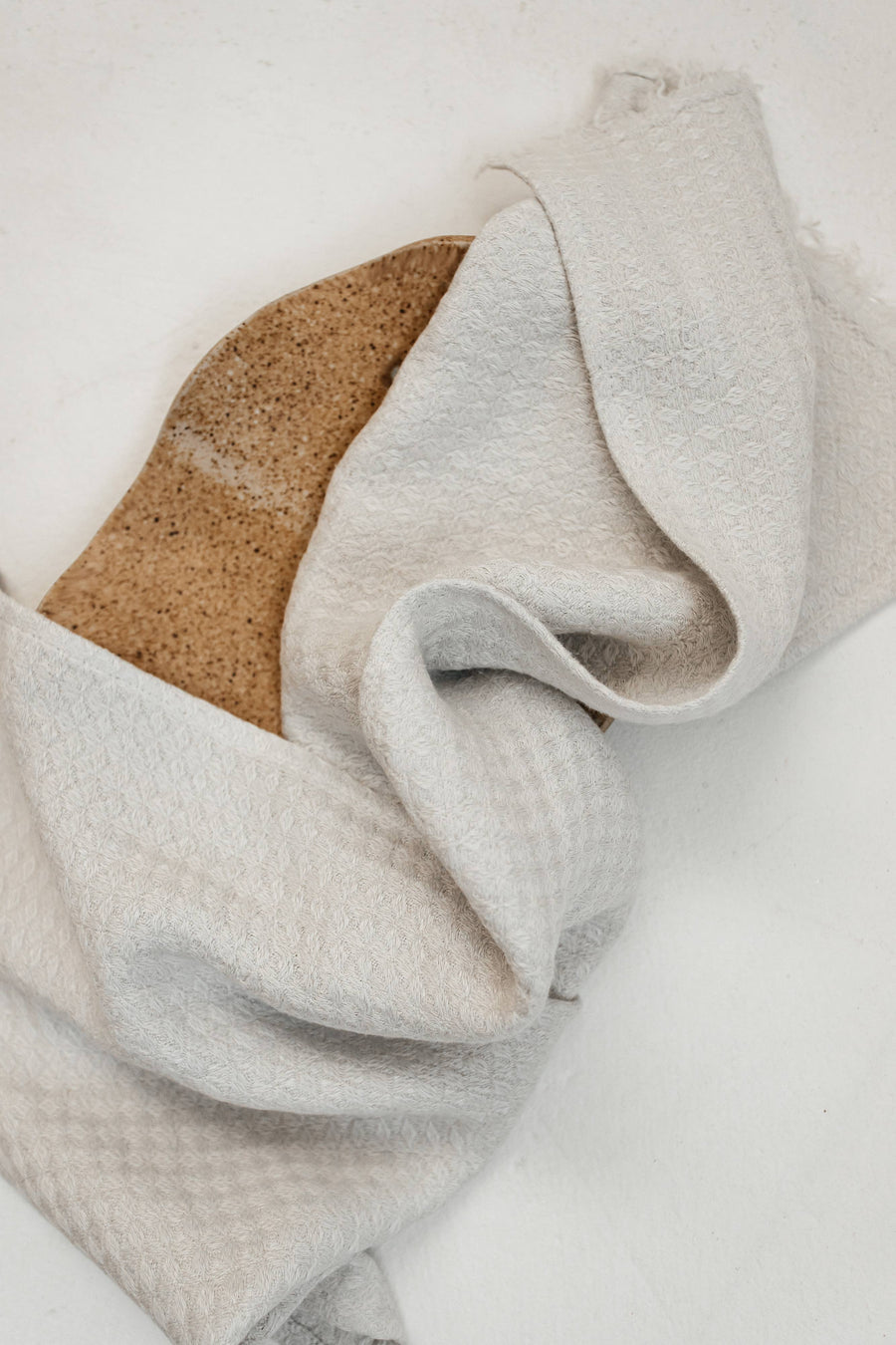 Folded light gray towel on a white surface folded over a wooden plate.