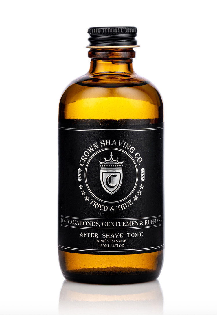 This image features a brown glass bottle of Crown Shaving Co. After Shave Tonic. The black label prominently displays the brand's logo and the product name, "AFTER SHAVE TONIC." The bottle is set against a white background.