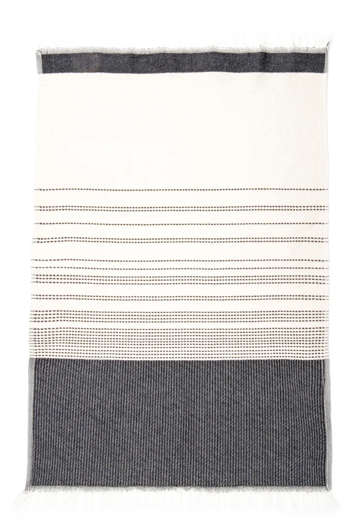 A white cotton Turkish towel with a wide dark gray band at the bottom, a narrower dark gray band at the top, and thin horizontal dashed dark gray stripes across the middle section. The towel has short, twisted fringe at both ends.