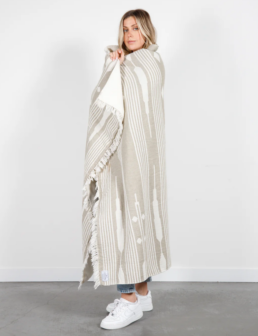 A woman wrapped in a khaki and white patterned throw blanket.