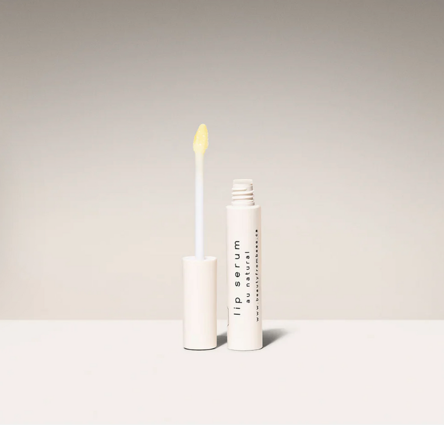 A white tube of "Lip Serum Au Natural" by Beauty from Bees, shown open with the applicator wand held upright to reveal the clear, glossy serum.