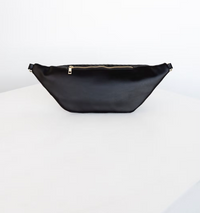 Thumbnail for The exterior back of the black fanny pack with a shiny finish and a gold zipper rests on a white surface.