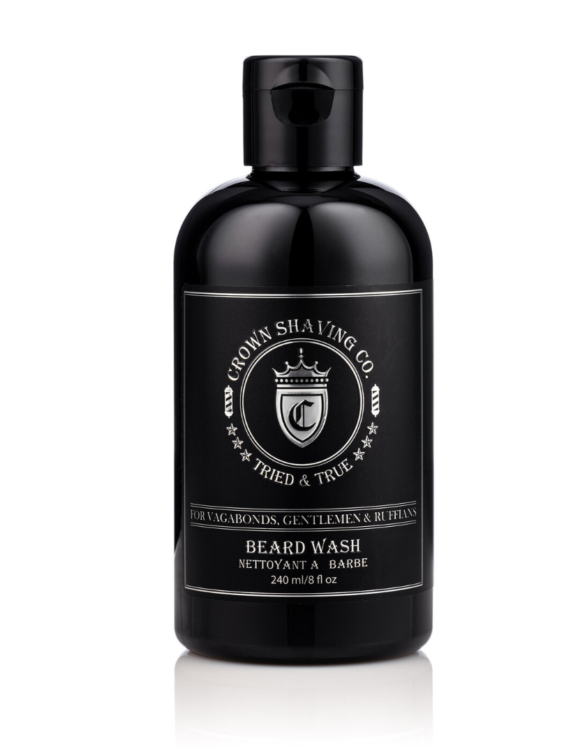 This image features a black bottle of Crown Shaving Co. Beard Wash. The label prominently displays the brand's logo and the product name "BEARD WASH NETTOYANT A BARBE." The bottle has a black cap.