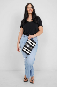 Thumbnail for A smiling woman in a black t-shirt and light-wash ripped jeans holds the small Black/Ecru striped Mercer Wet-Dry bag as a clutch.