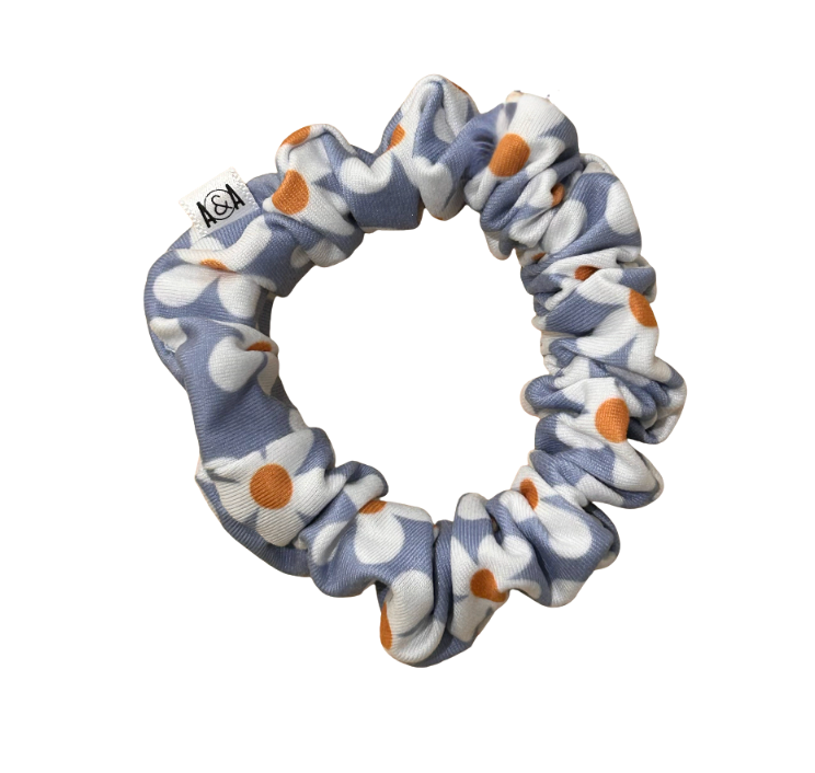 Light blue scrunchie with a repeating pattern of white daisy flowers with bright orange centers.