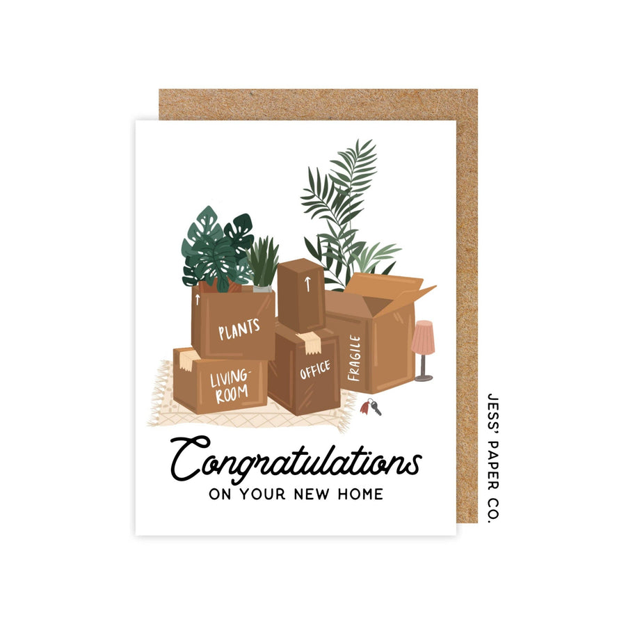 A vertical greeting card showing a stack of moving boxes, some labeled "PLANTS," "LIVING ROOM," "OFFICE," and "FRAGILE," with a lamp and keys. Below, it reads "Congratulations ON YOUR NEW HOME." "JESS' PAPER CO." is on the right.