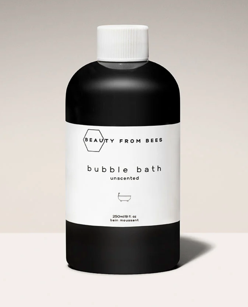 
A close-up of a small, black bottle of "Beauty From Bees" bubble bath with a white cap and a white label, indicating it is "unscented."