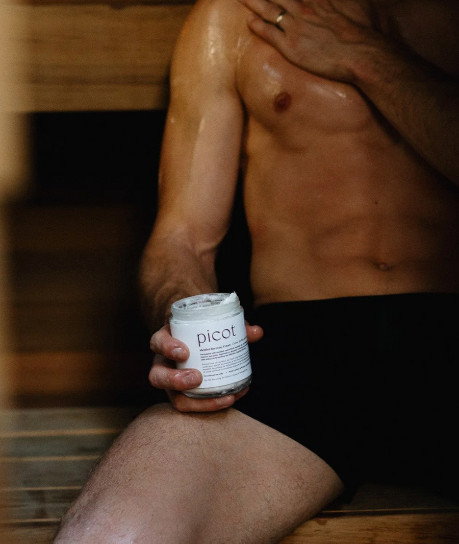  close-up shot of a person's legs, abs, and chest in what looks like a sauna. The person is holding a jar of "picot Menthol Recovery Cream" and has applied the cream to their shoulders and biceps.