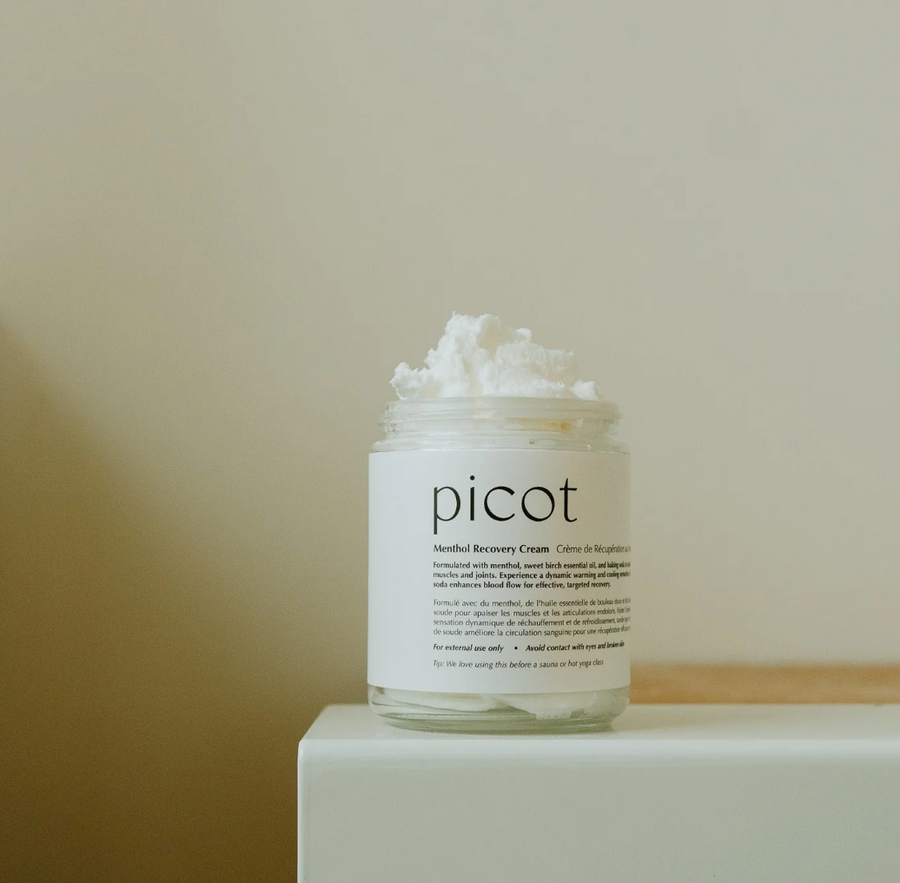 A jar of "picot Menthol Recovery Cream" with a generous scoop of the white cream visible on top. The jar is sitting on a white and light beige surface.