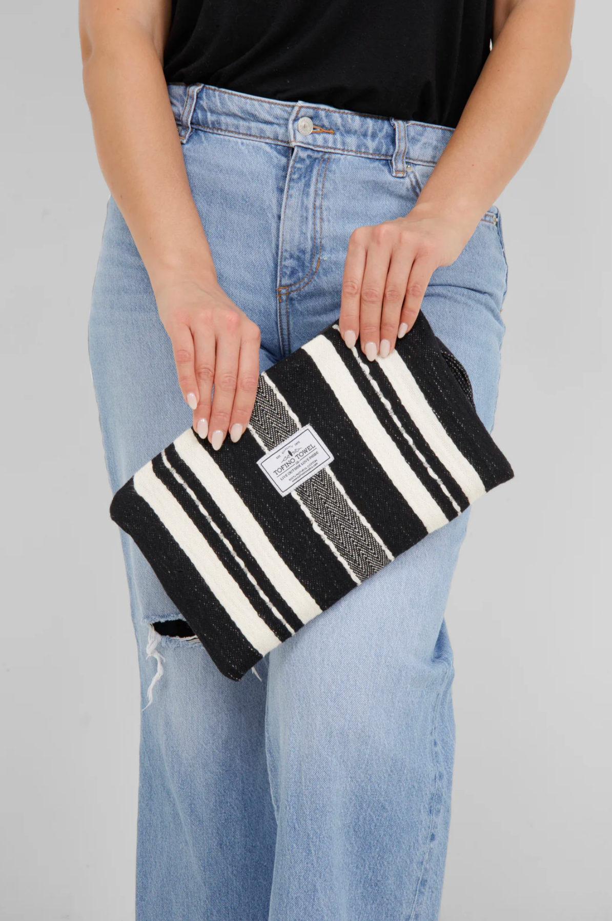 A close-up of a person holding the small Black/Ecru striped Turkish cotton bag, highlighting the hand-embroidered details and Tofino Towel Co. logo
