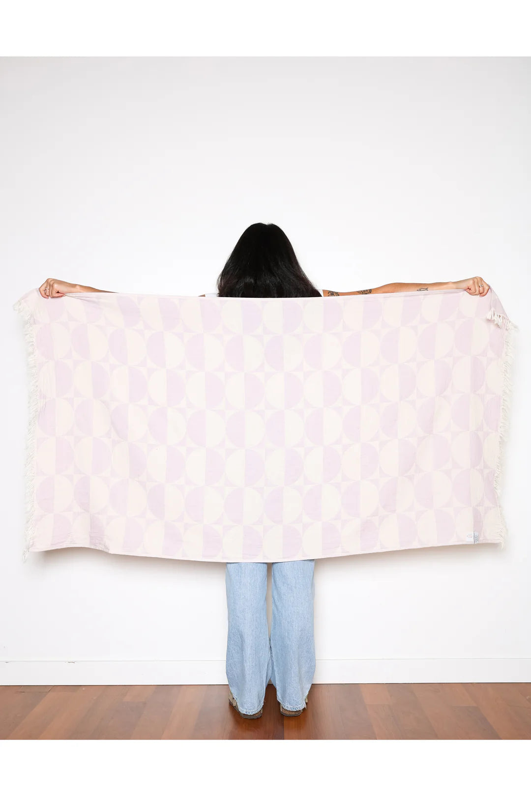 A woman holding the lilac Phase towel spread wide across her back, showcasing its generous 160cm length and bold geometric circular pattern.