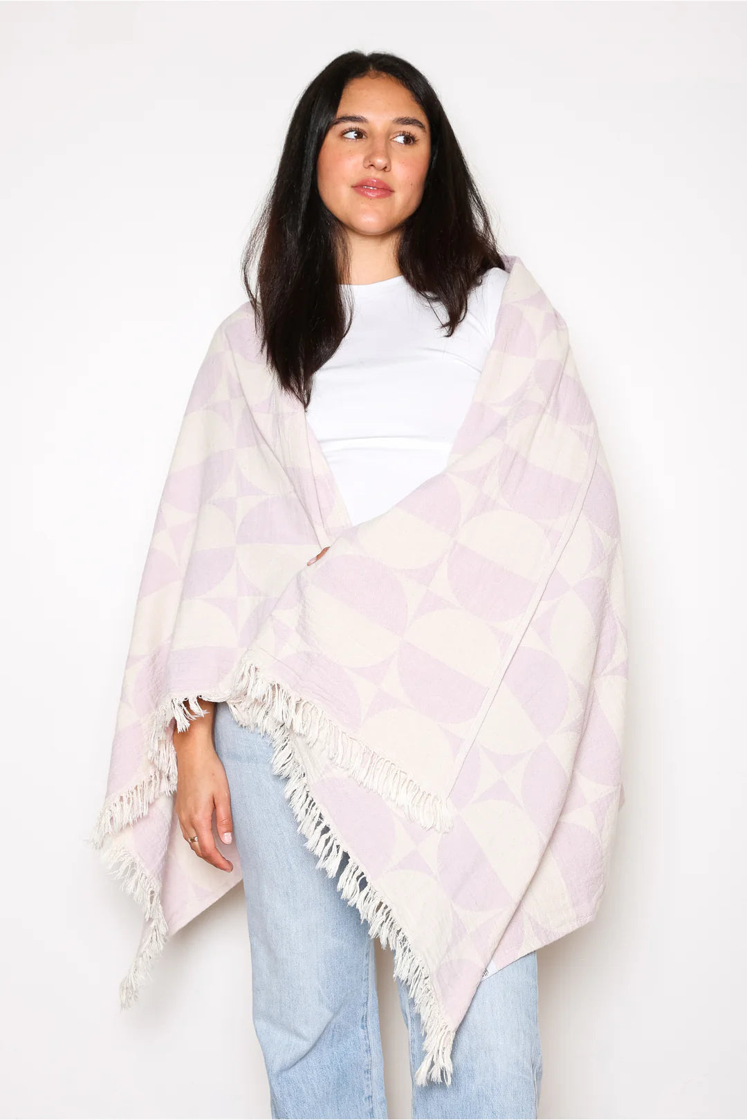 A woman draped in the lilac Phase towel like a shawl, demonstrating its soft, lightweight texture. The towel covers her shoulders and torso, held against a white t-shirt and light blue jeans.