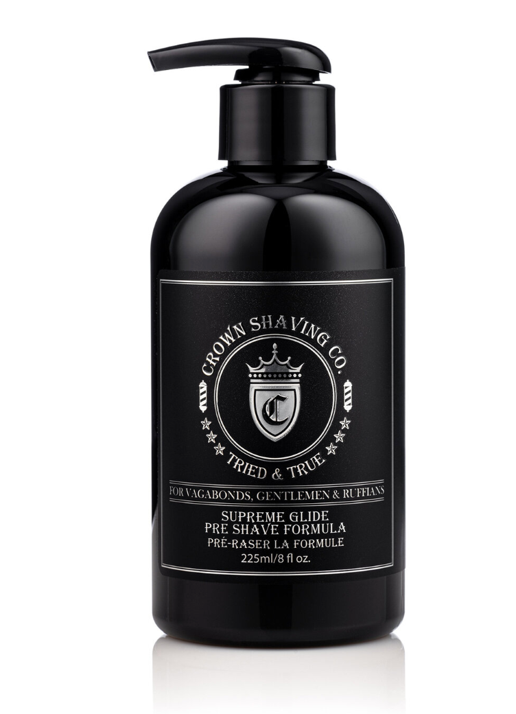 This image features a black pump bottle of Crown Shaving Co. Supreme Glide Pre-Shave Formula. The label prominently displays the brand's logo and the product name "SUPREME GLIDE PRE SHAVE FORMULA PRÉ-RASER LA FORMULE." The bottle has a black pump dispenser.