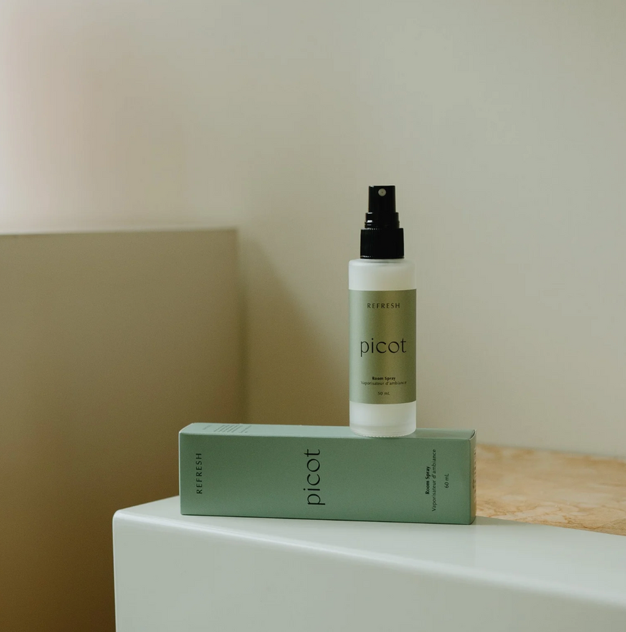A light green box labeled "picot refresh Room Spray" sits on a white surface with a matching bottle standing upright on top of it.