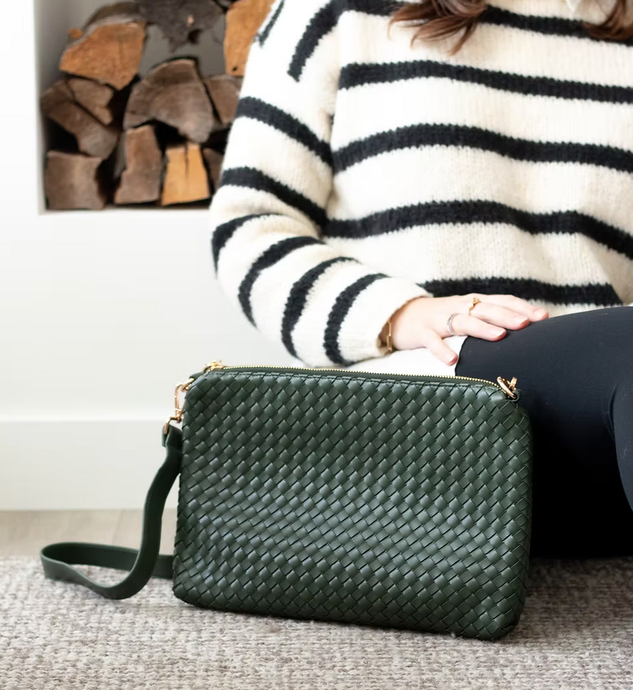 A green woven bag is positioned next to a woman wearing leggings and white/black horizontal striped sweater sitting on the floor. 