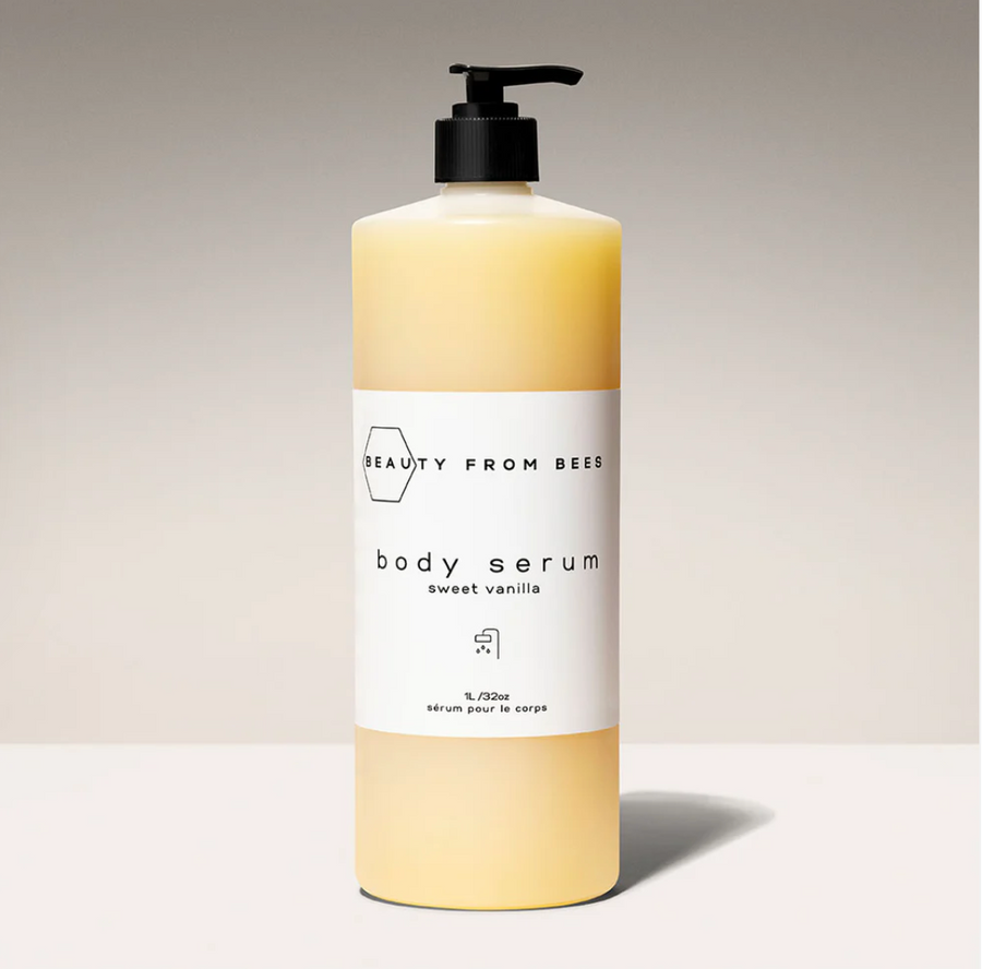 A light yellow bottle of Beauty From Bees sweet vanilla body serum with a black label. The bottle has a black pump dispenser.