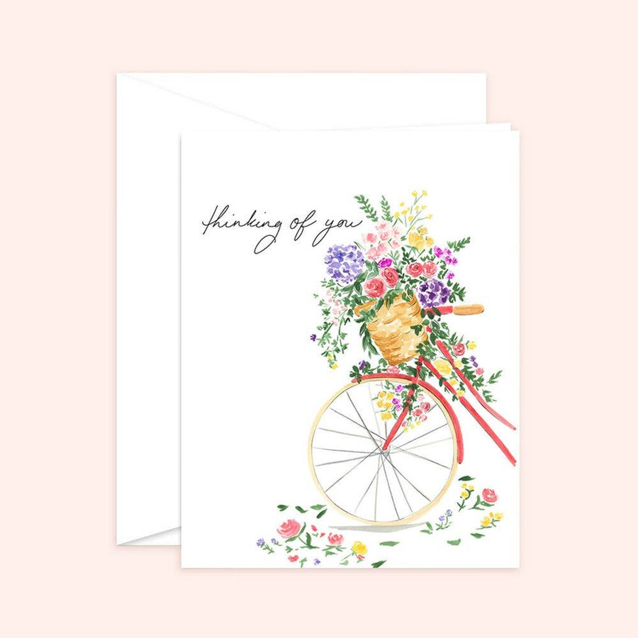 Watercolor illustration of a vintage red bicycle with a basket overflowing with colorful spring flowers, featuring the handwritten text "thinking of you."