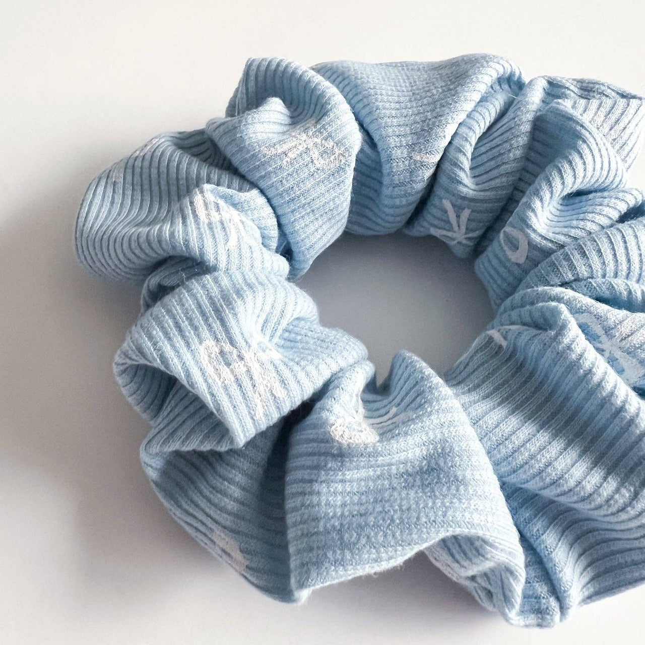 A light blue scrunchie with a ribbed texture and small white bow-tie shapes.