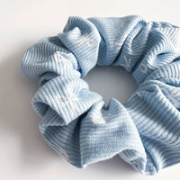 Thumbnail for A light blue scrunchie with a ribbed texture and small white bow-tie shapes.