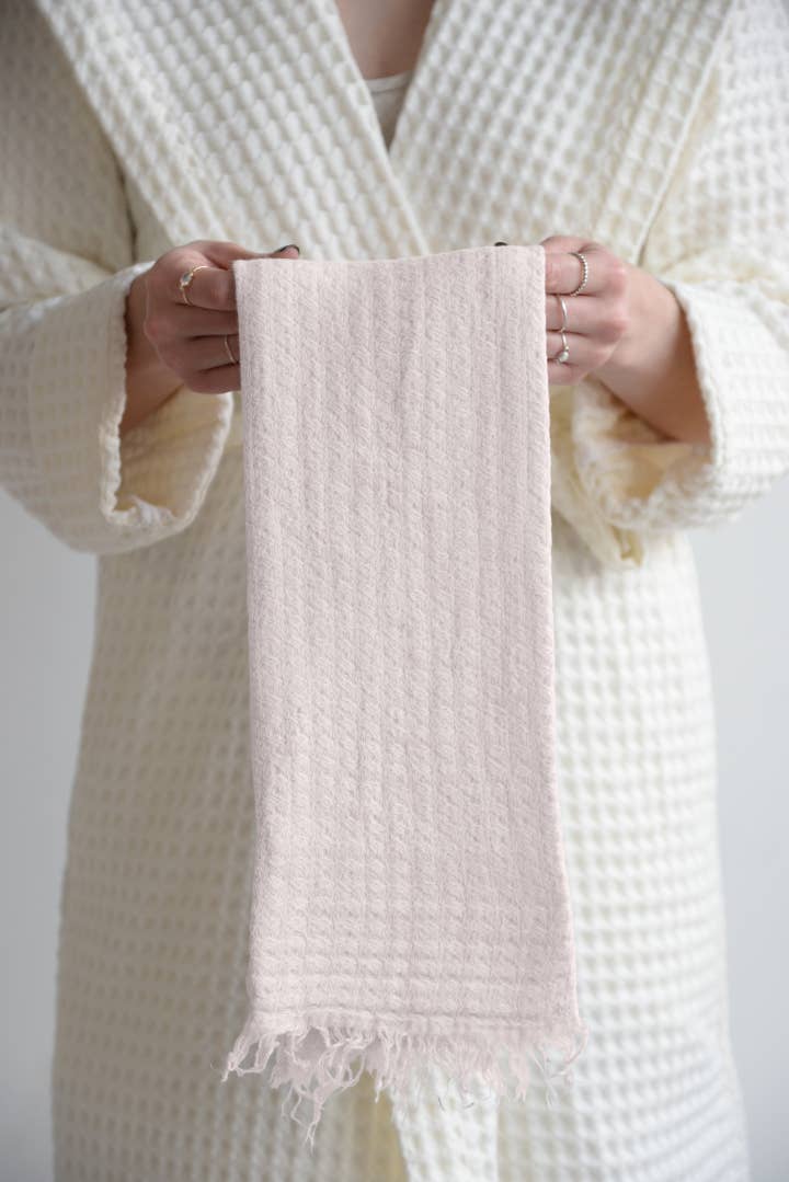 A person wearing a cream waffle robe wearing a textured white robe holding a matching towel.