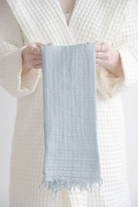 Thumbnail for A person wearing a cream waffle robe holding a light blue textured towel with a white background