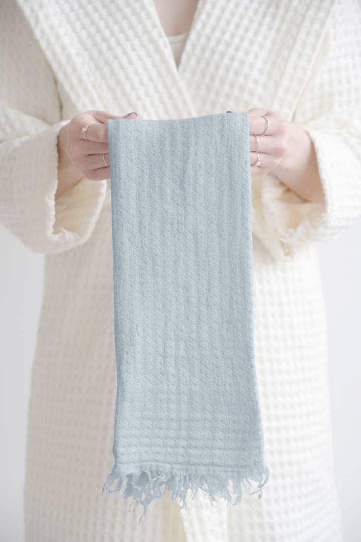 A person wearing a cream waffle robe holding a light blue textured towel with a white background