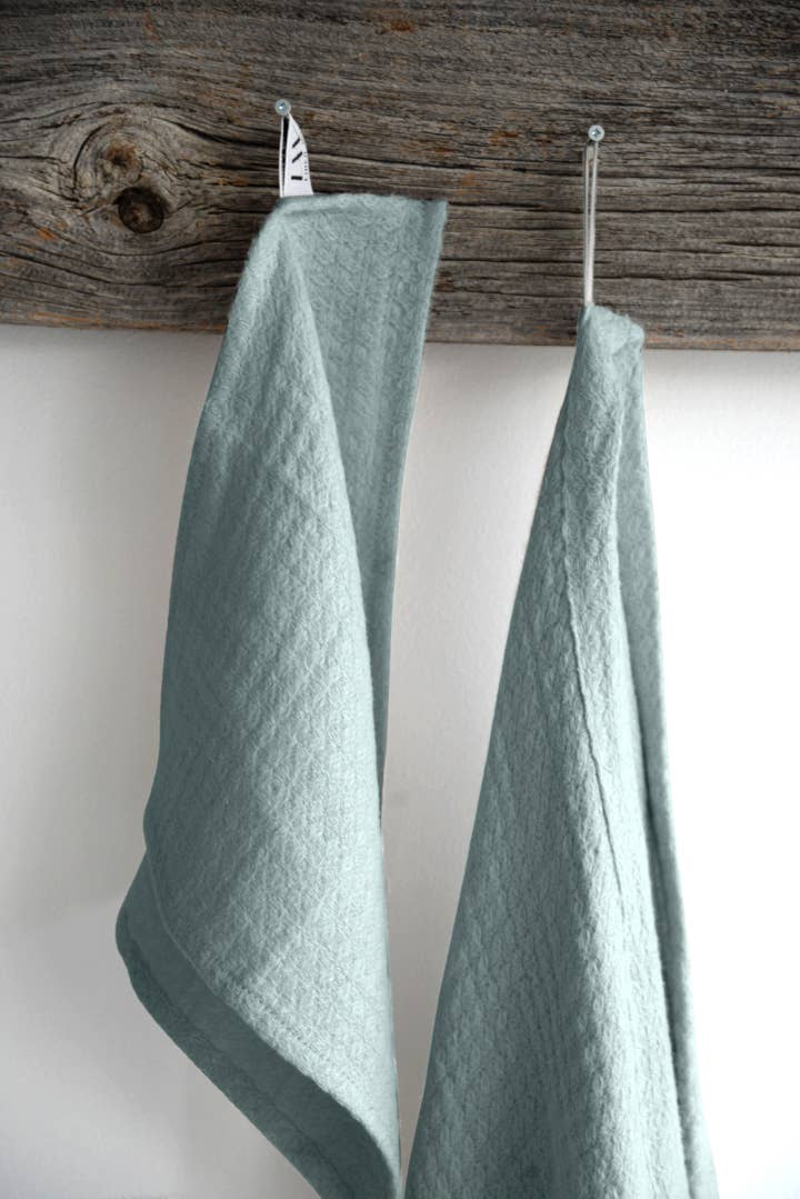 A light teal wash cloth and a matching hand towel hangs on a wooden rod against a white wall. 