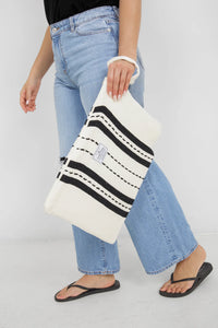 Thumbnail for A side-view of a person walking while holding the large Ecru/Black striped Mercer bag by its wrist strap. The bag hangs lower and appears significantly more spacious than the small version, reaching from the waist down to the mid-thigh.