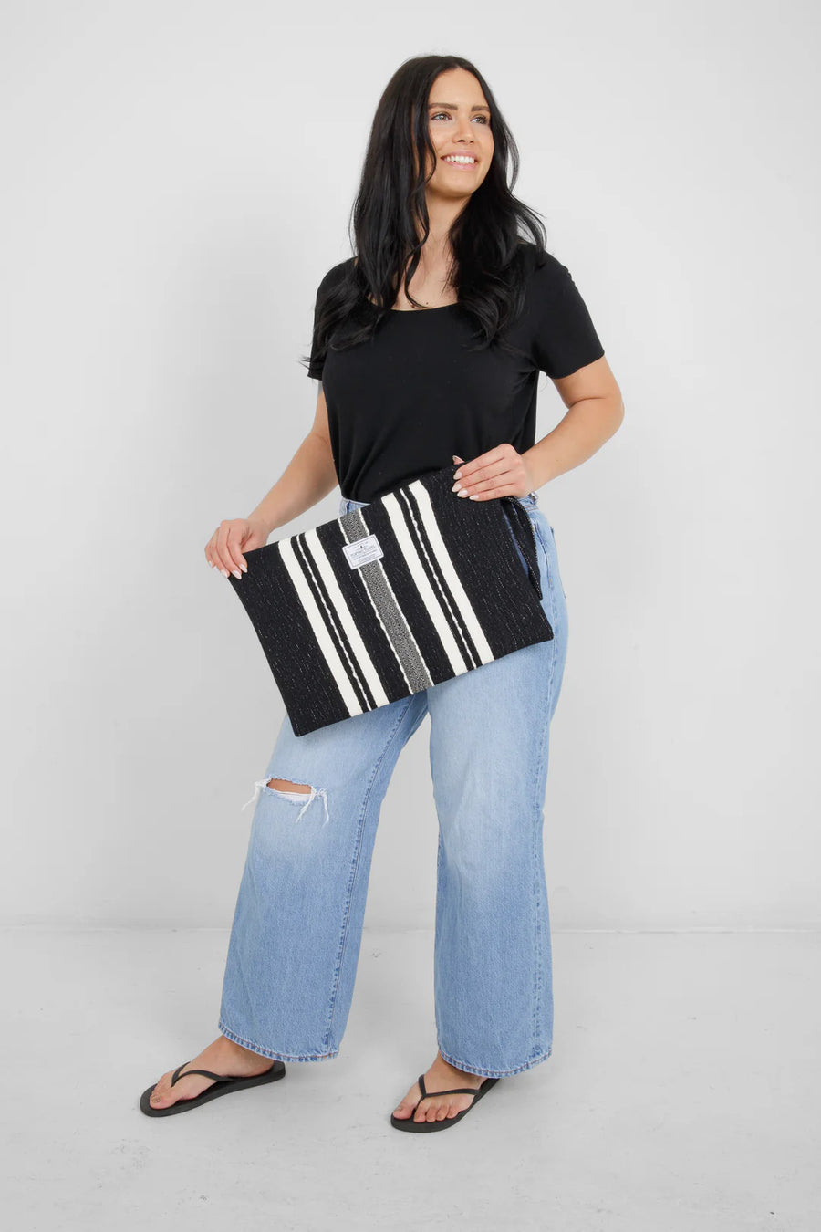 A person holding the large Black/Ecru striped Mercer bag horizontally with both hands. The bag’s wide dimensions are clear as it covers the width of the torso, held against a black t-shirt and light-wash jeans.